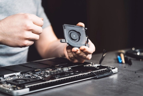 The image shows a technician carefully removing a cooling fan from a laptops
