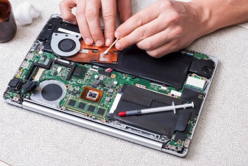 The image shows a technician working on the internal components of a laptop, likely performing maintenance or repair