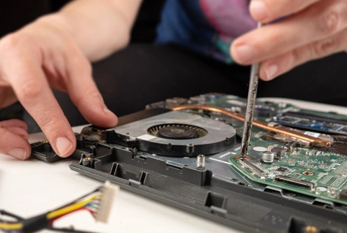 The image shows a technician working on a laptop, using a screwdriver to remove or adjust the cooling fan.