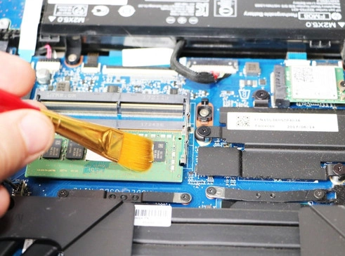 Why Choose Our Computer Repair in Abbotsford alt The image shows a technician carefully cleaning the internal components of a laptop, specifically using a small brush to remove dust from the memory (RAM) module on the moth