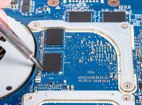 The image shows a close-up view of a technician using precision tweezers to handle a component on a laptop's motherboard.