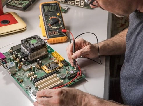 The image shows a technician using a multimeter to test the components of a computer motherboard