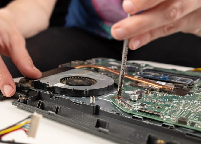 Close-up of a person using a tool to unscrew or work near the cooling fan and heat sink area of a laptop motherboard